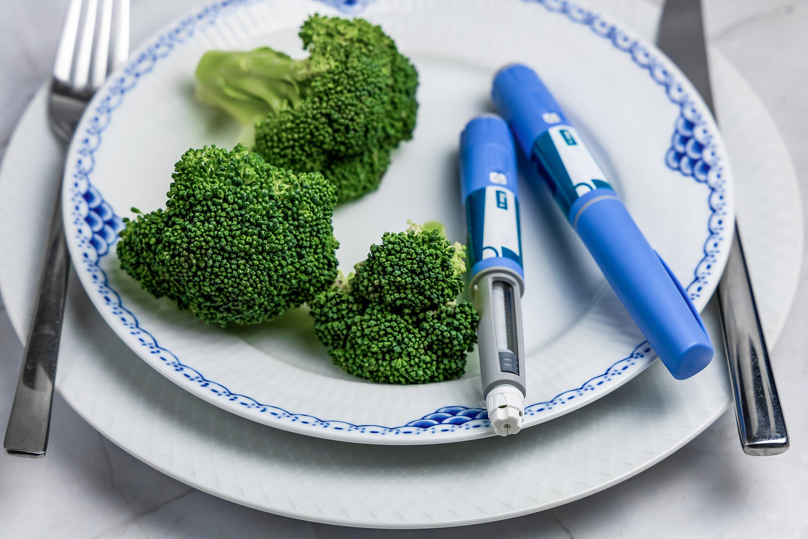 Two Ozempic pens sitting on a plate with tree pieces of broccoli (Photo Credit: Shutterstock)